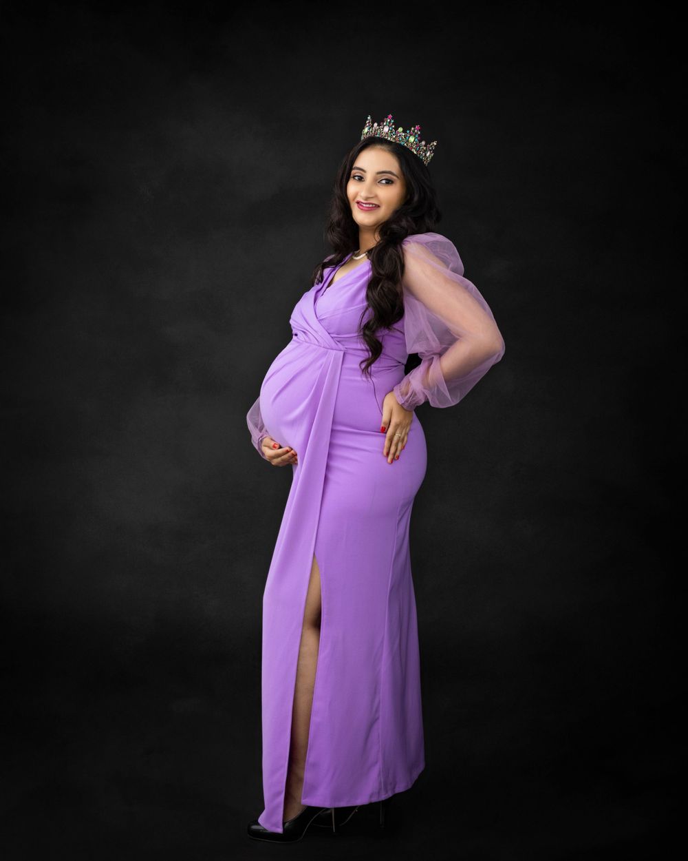 Maternity portrait in purple gown with crown against dark background.