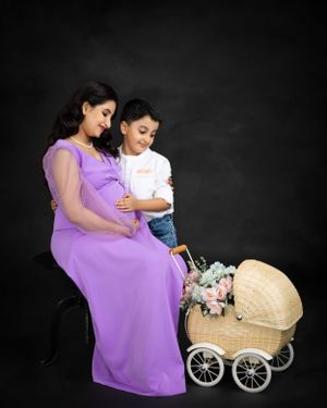 Mother-to-be in purple gown shares moment with child next to decorative carriage.