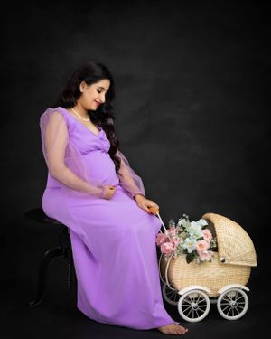 Maternity photo with woman in purple dress seated beside vintage style pram.
