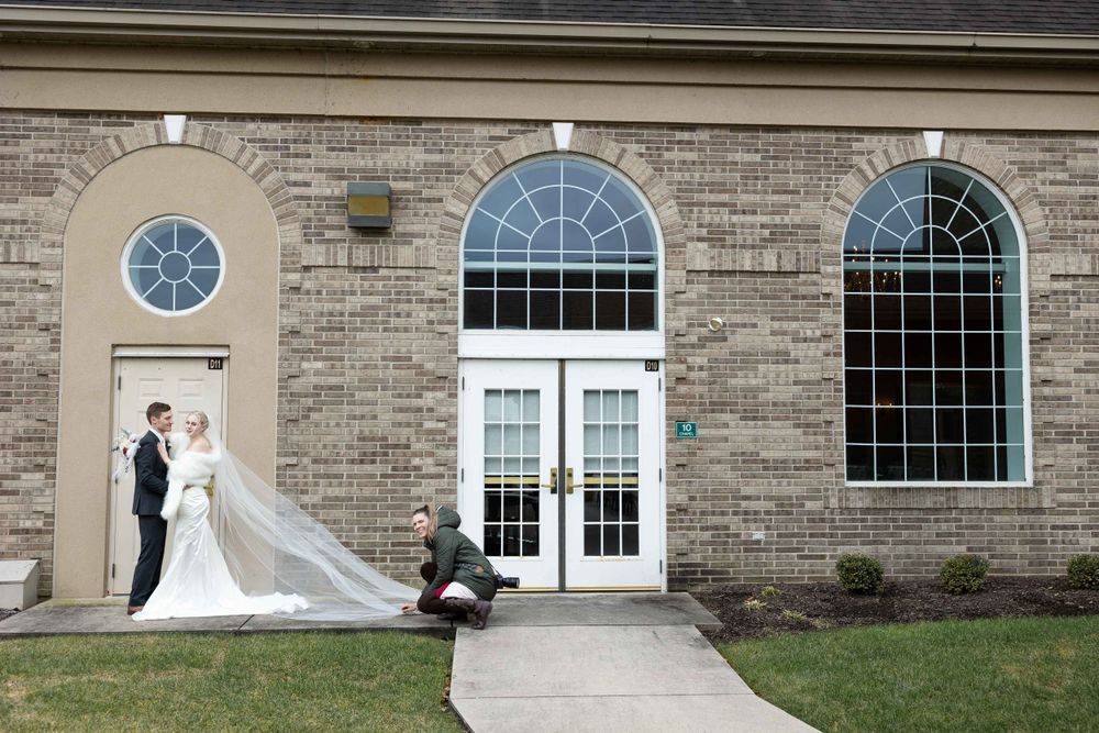 Elegant wedding photo outside brick building with flowing veil in architectural setting.
