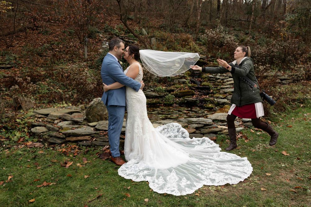 Autumn wedding scene with long flowing train against rustic stone backdrop.