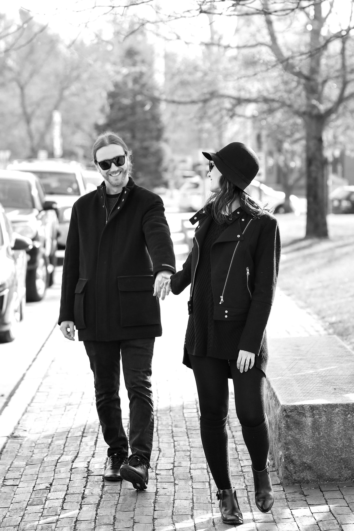 Stylish couple in black coats walking down brick sidewalk in winter.