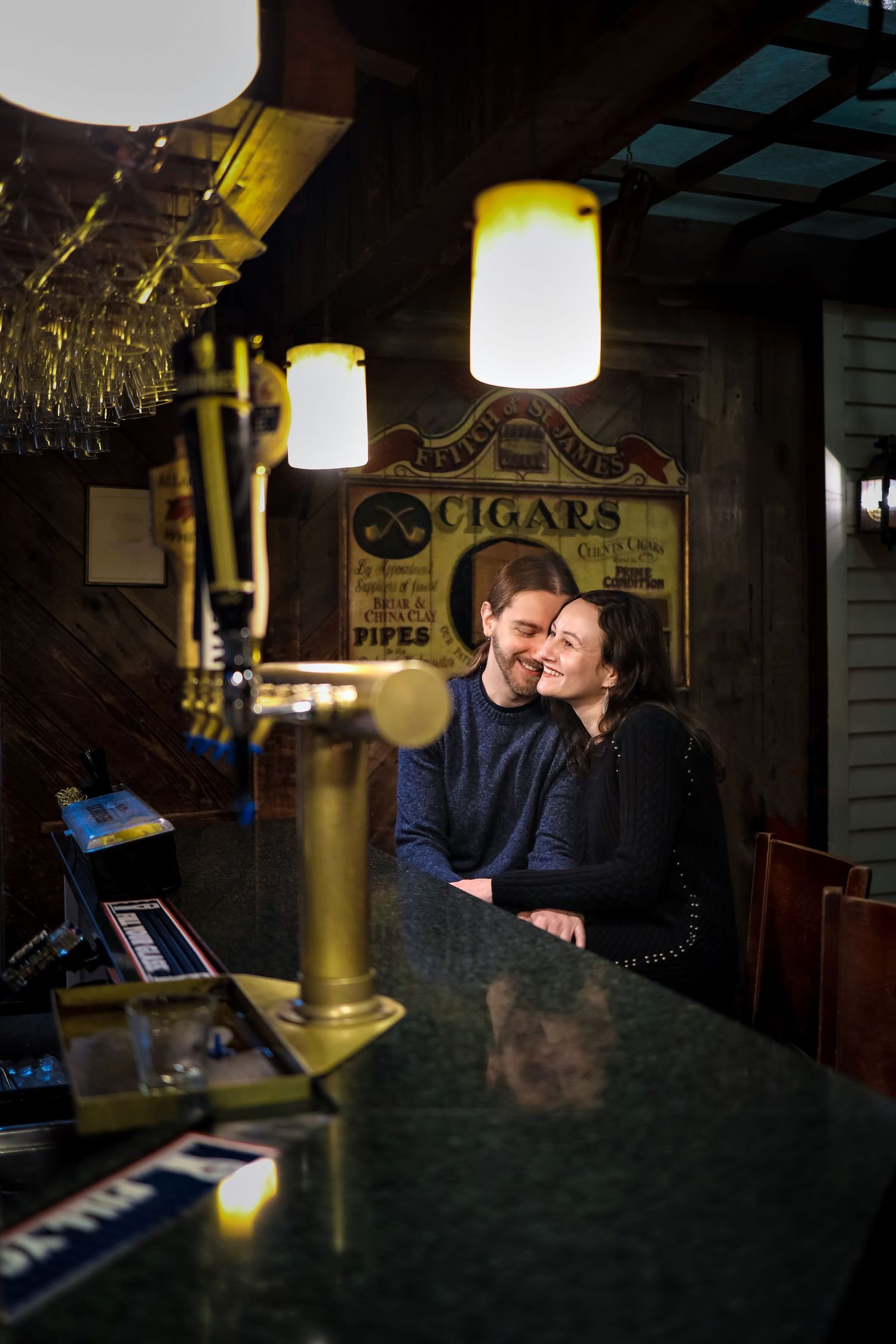Couple sharing romantic moment at dimly lit vintage bar with glowing pendant lights.