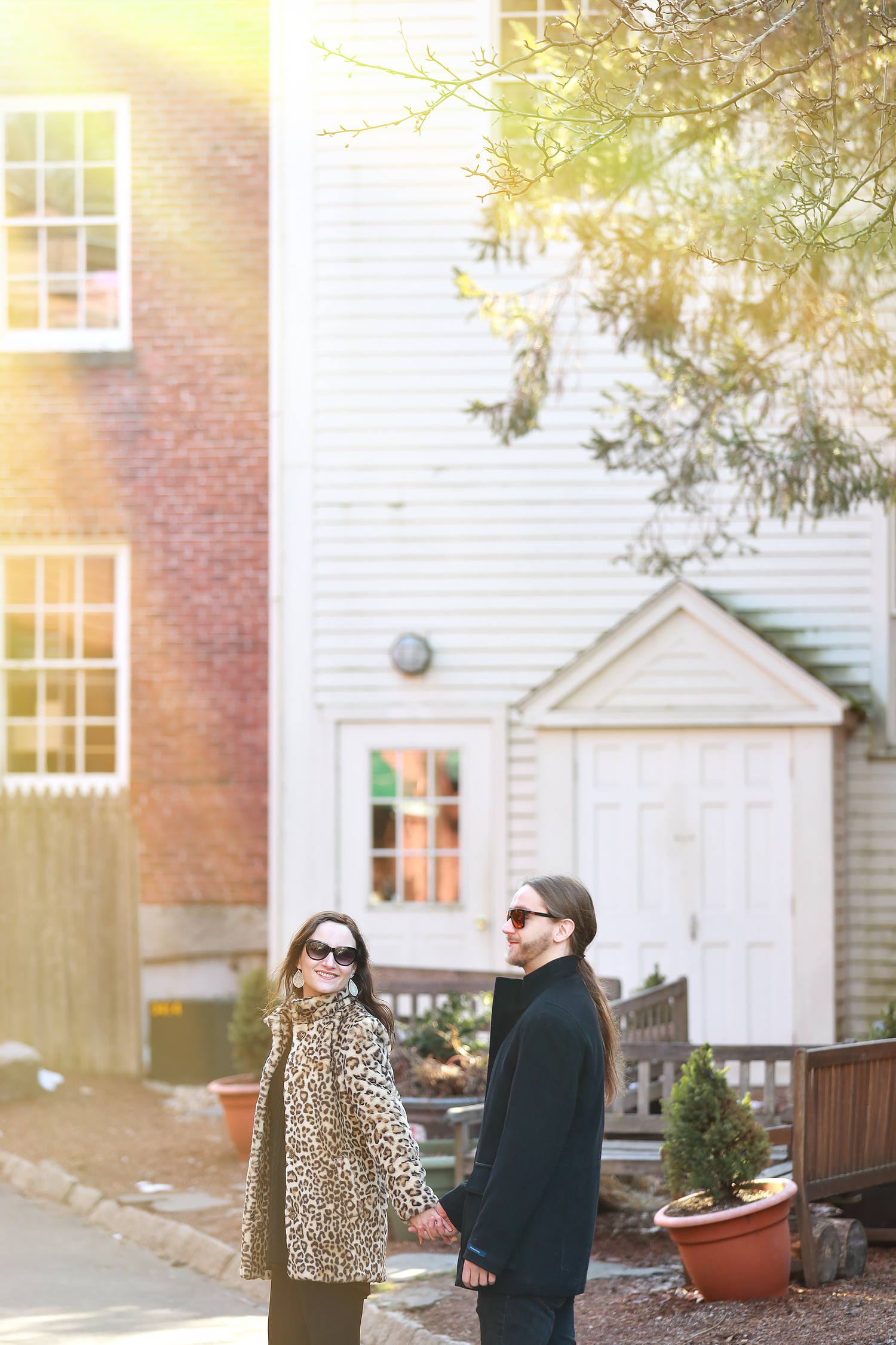 Stylish couple standing outside historic brick building in warm sunlight.