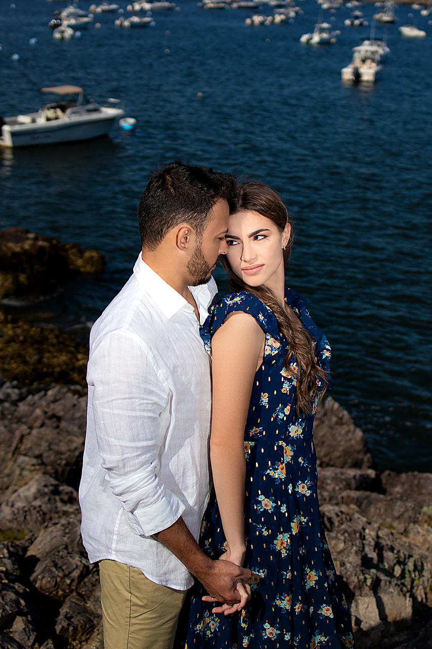 Couple poses against harbor backdrop with boats floating in blue water.