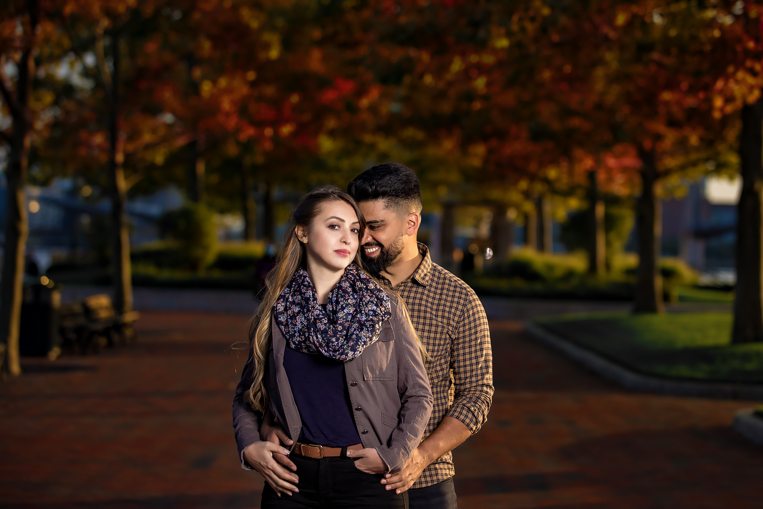 A romantic couple poses in an autumn park with colorful fall foliage in the background.