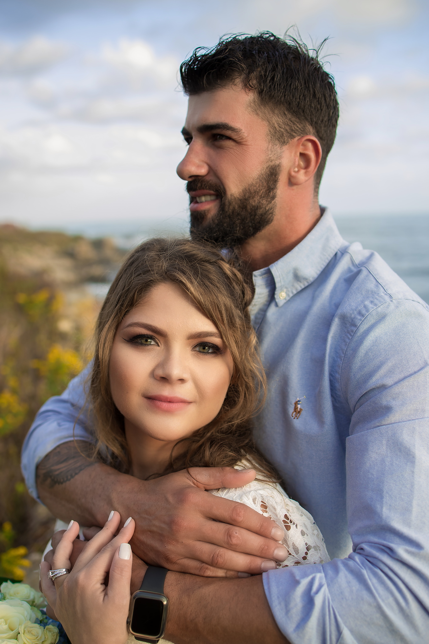 A romantic portrait of an embracing couple against a coastal background.