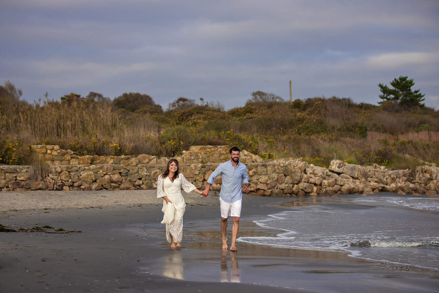 A couple walking along the shoreline at a scenic beach with cliffs and waves.