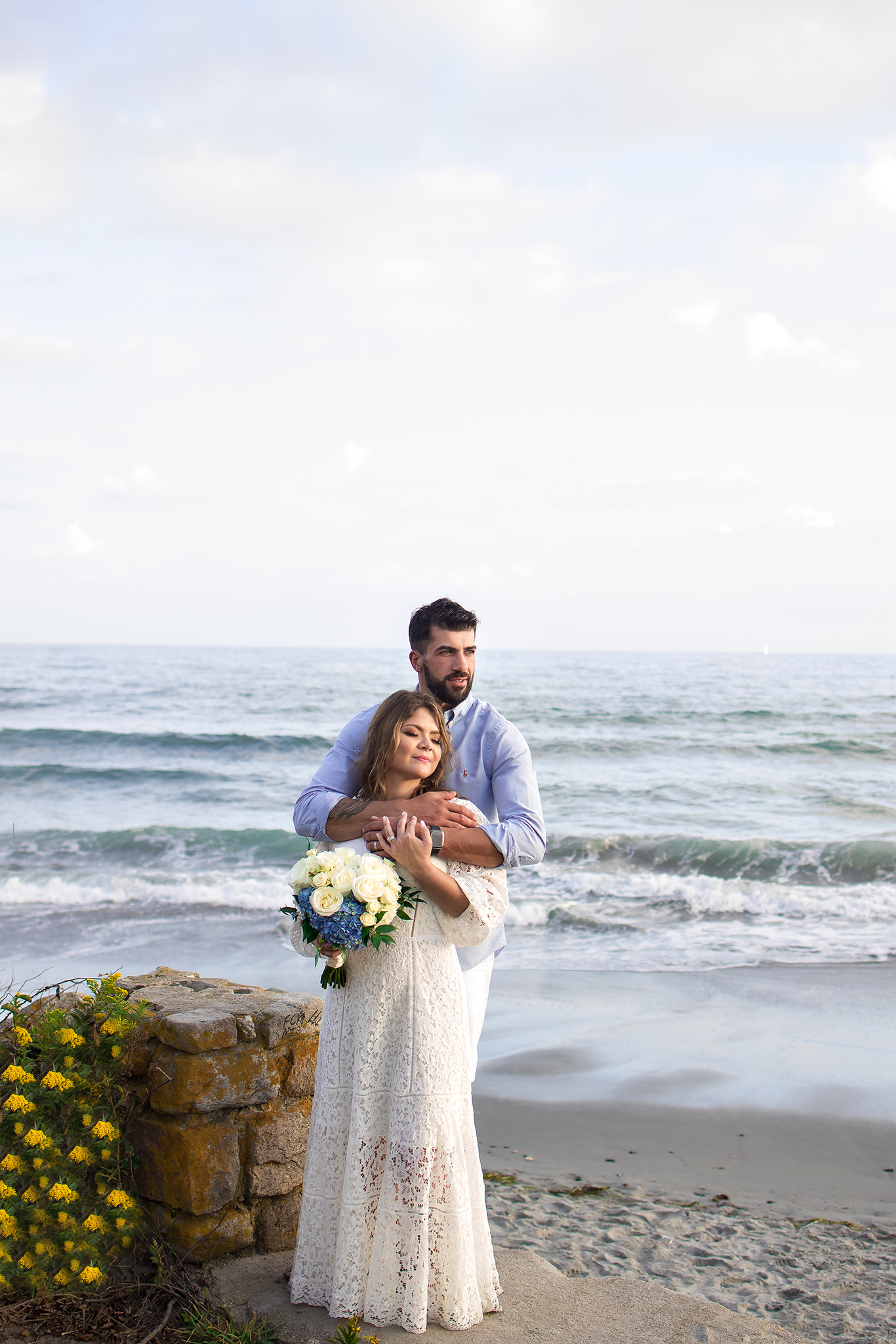 A romantic beach engagement session with yellow flowers and crashing waves in the background.