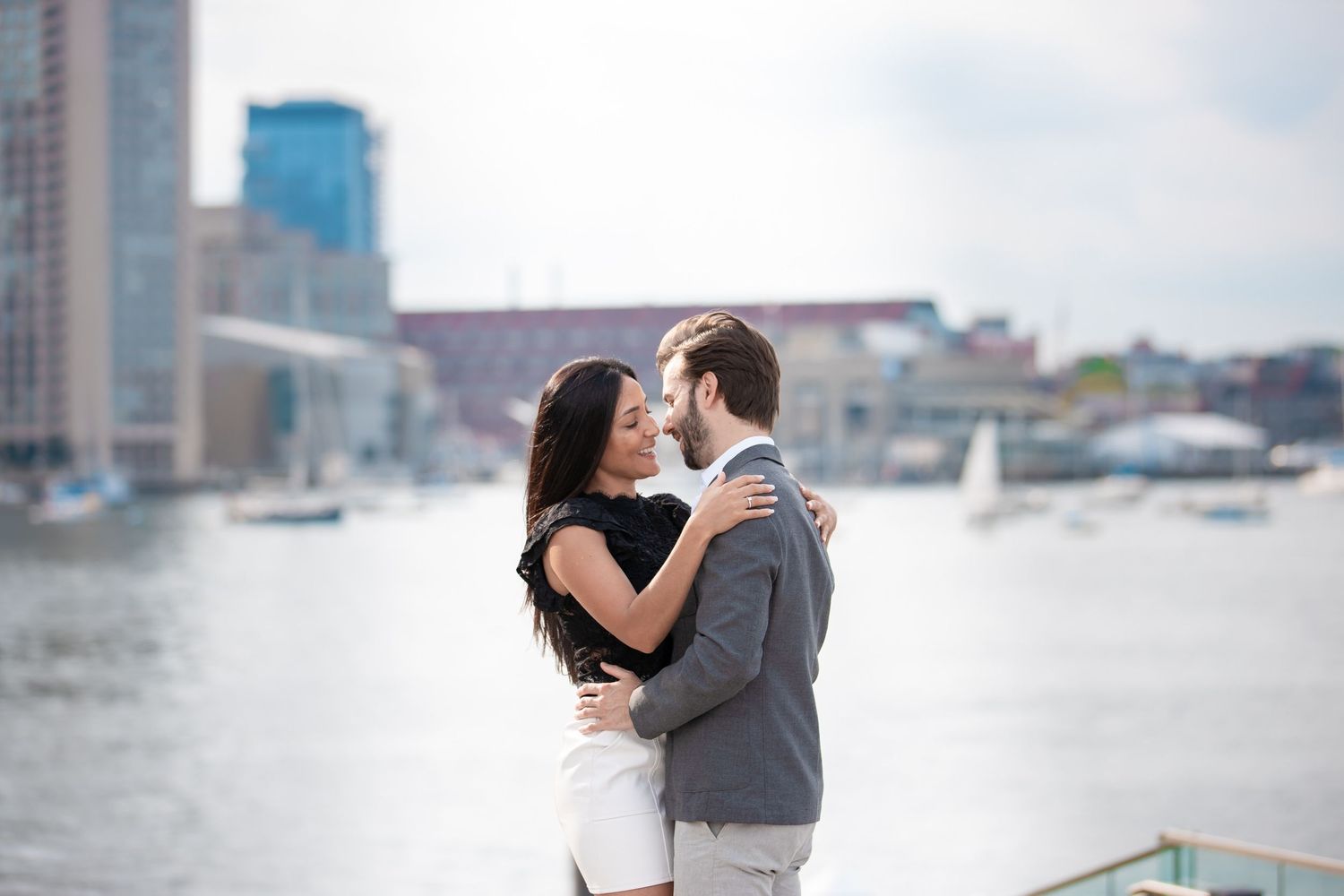 Couple shares intimate moment on waterfront with city skyline in background.