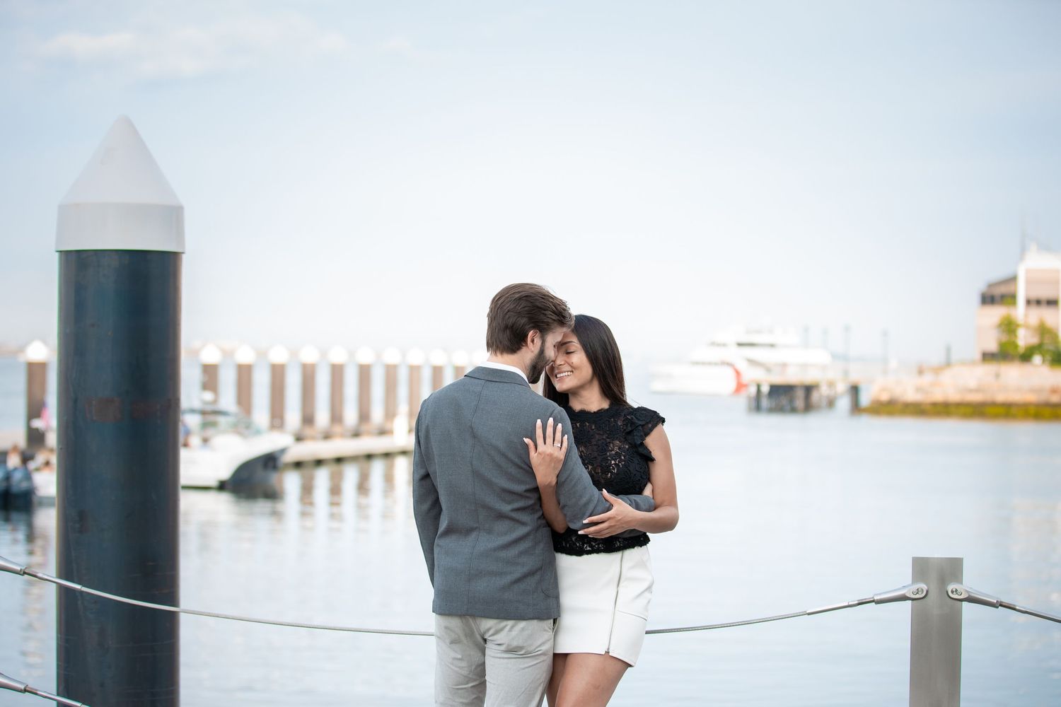 Couple sharing tender moment by marina dock with boats in background.