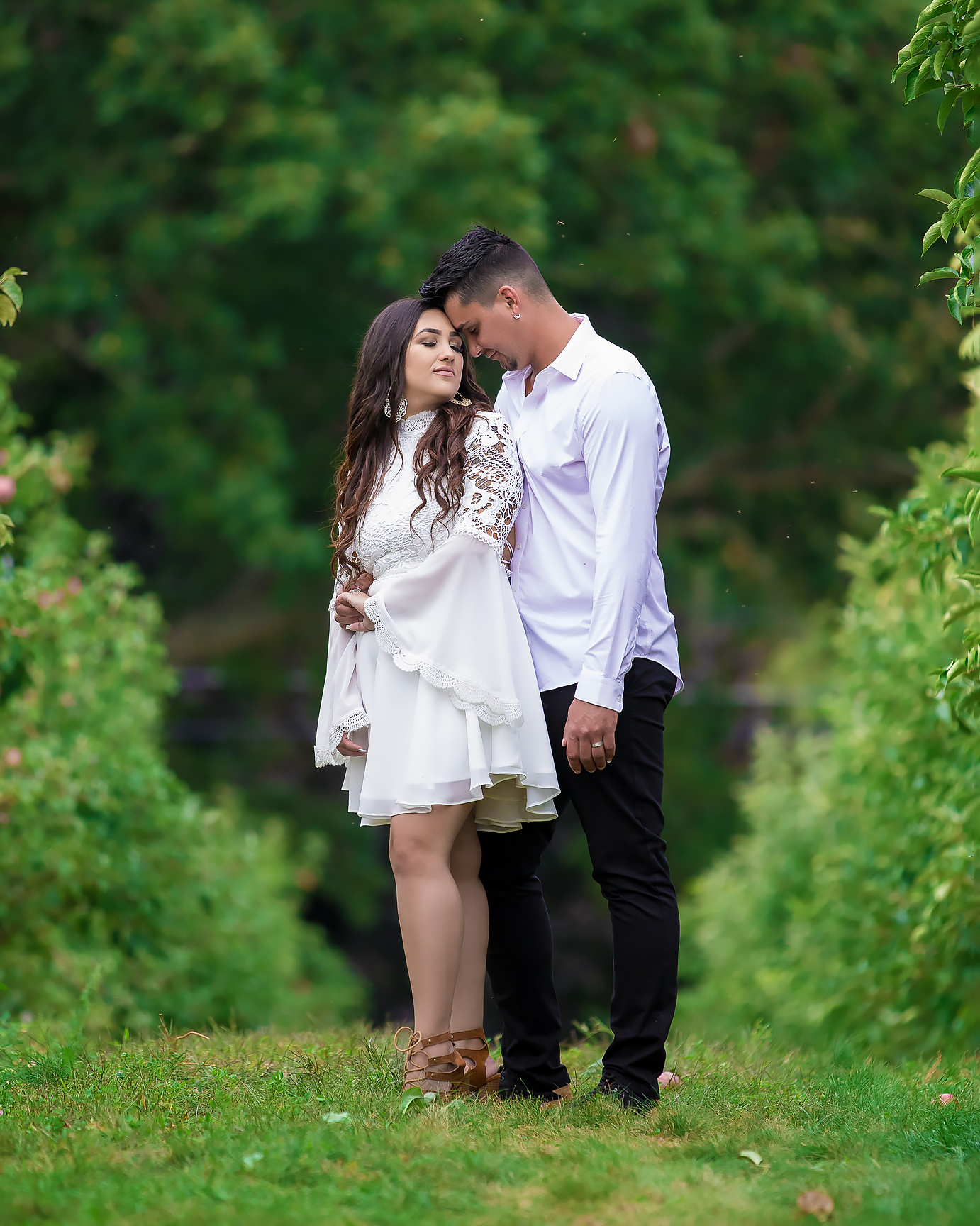 Romantic couple embraces in a lush garden path wearing white and dark casual attire.