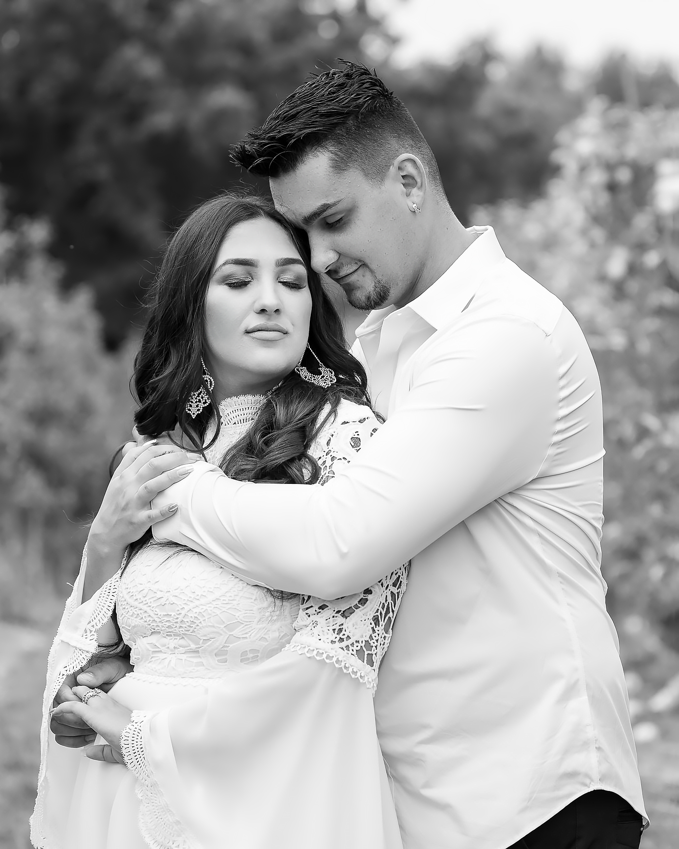Intimate black and white portrait of couple in white attire embracing outdoors.