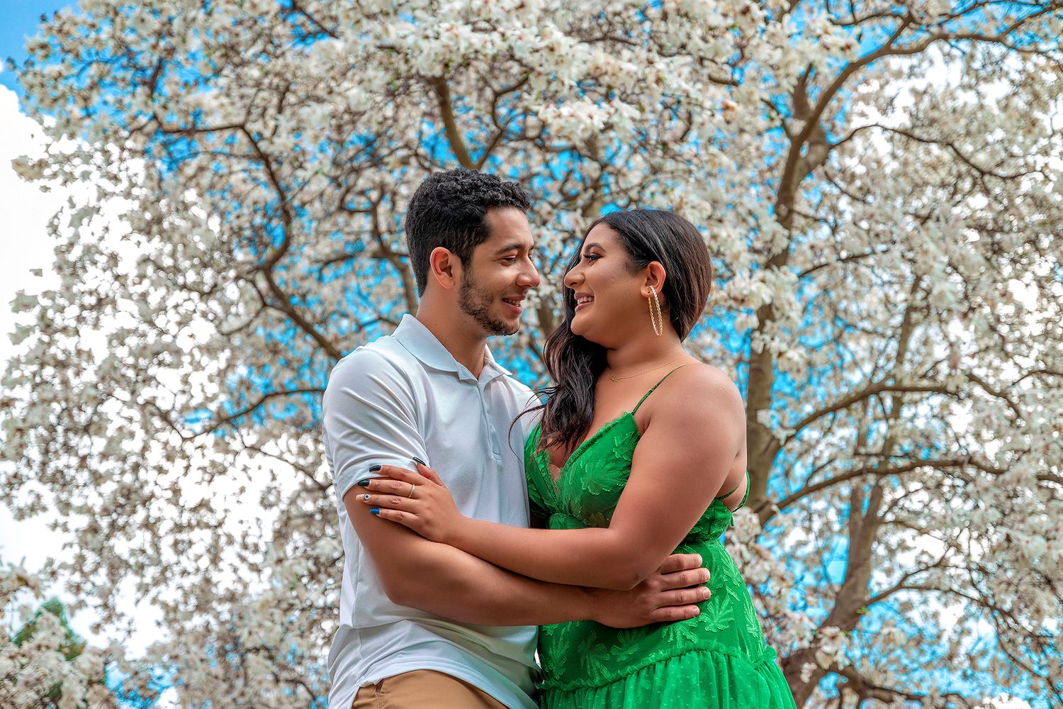 Couple embraces under blooming cherry blossom trees on a spring day.