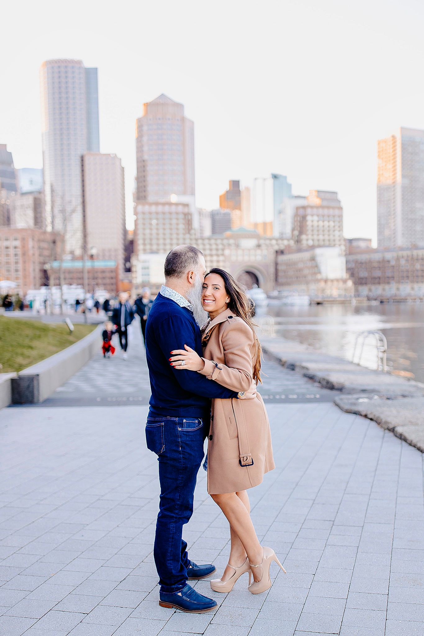 Romantic moment captured along city waterfront with Boston skyline in background.