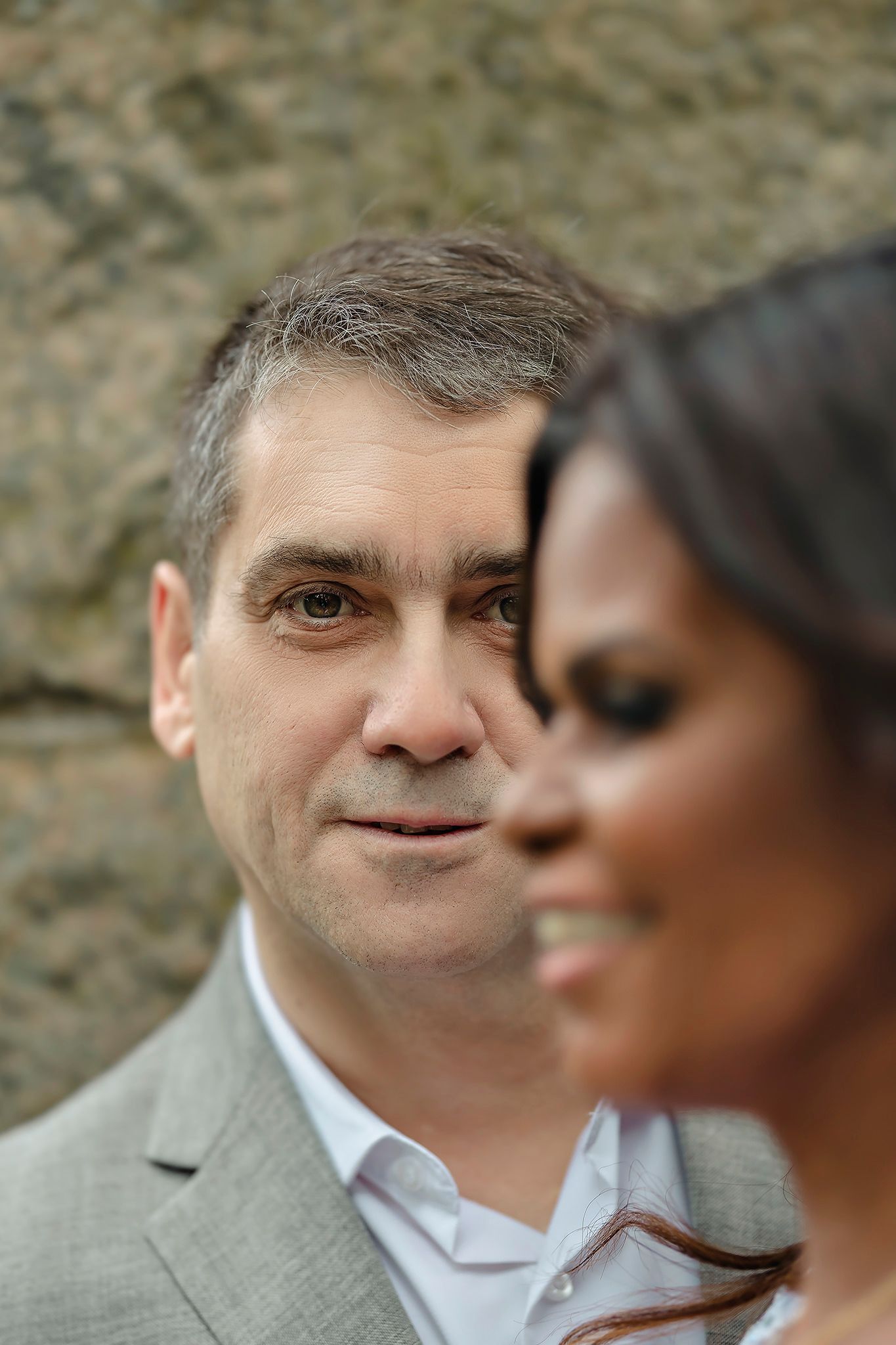 Close up side profile of newlyweds in formal attire against textured stone wall.