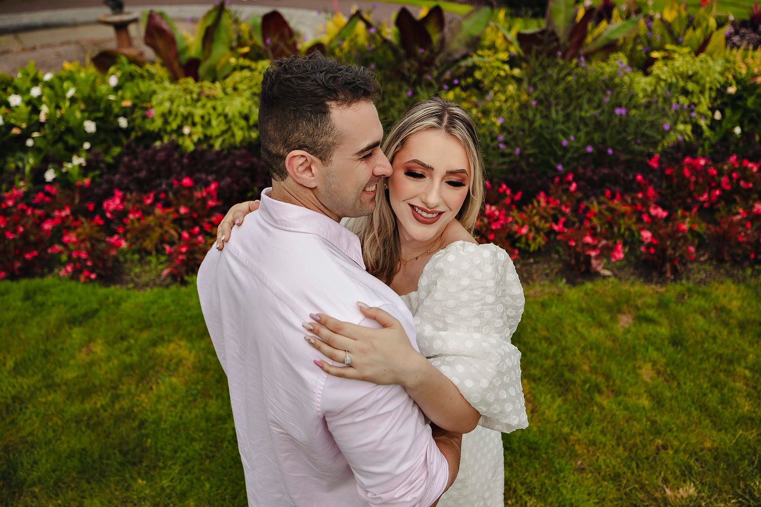 Romantic embrace in garden with colorful flowers in background.