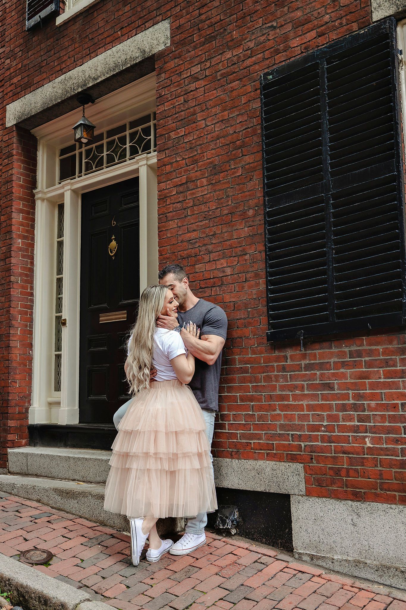 Romantic couple embracing on brick steps in front of classic brownstone doorway.