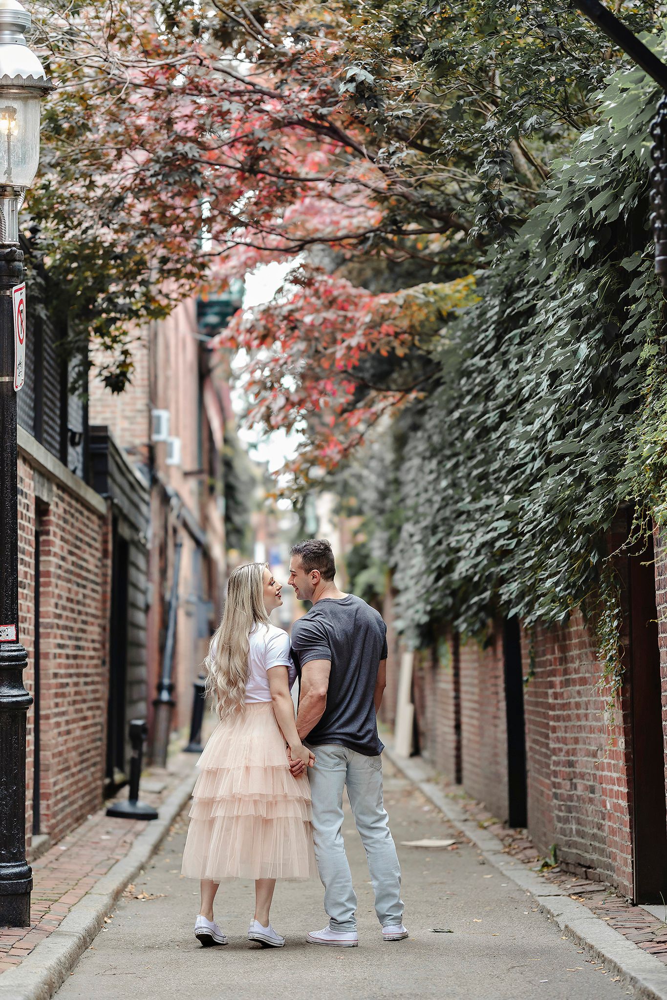 Couple walking hand in hand down a charming brick alley with blooming trees overhead.