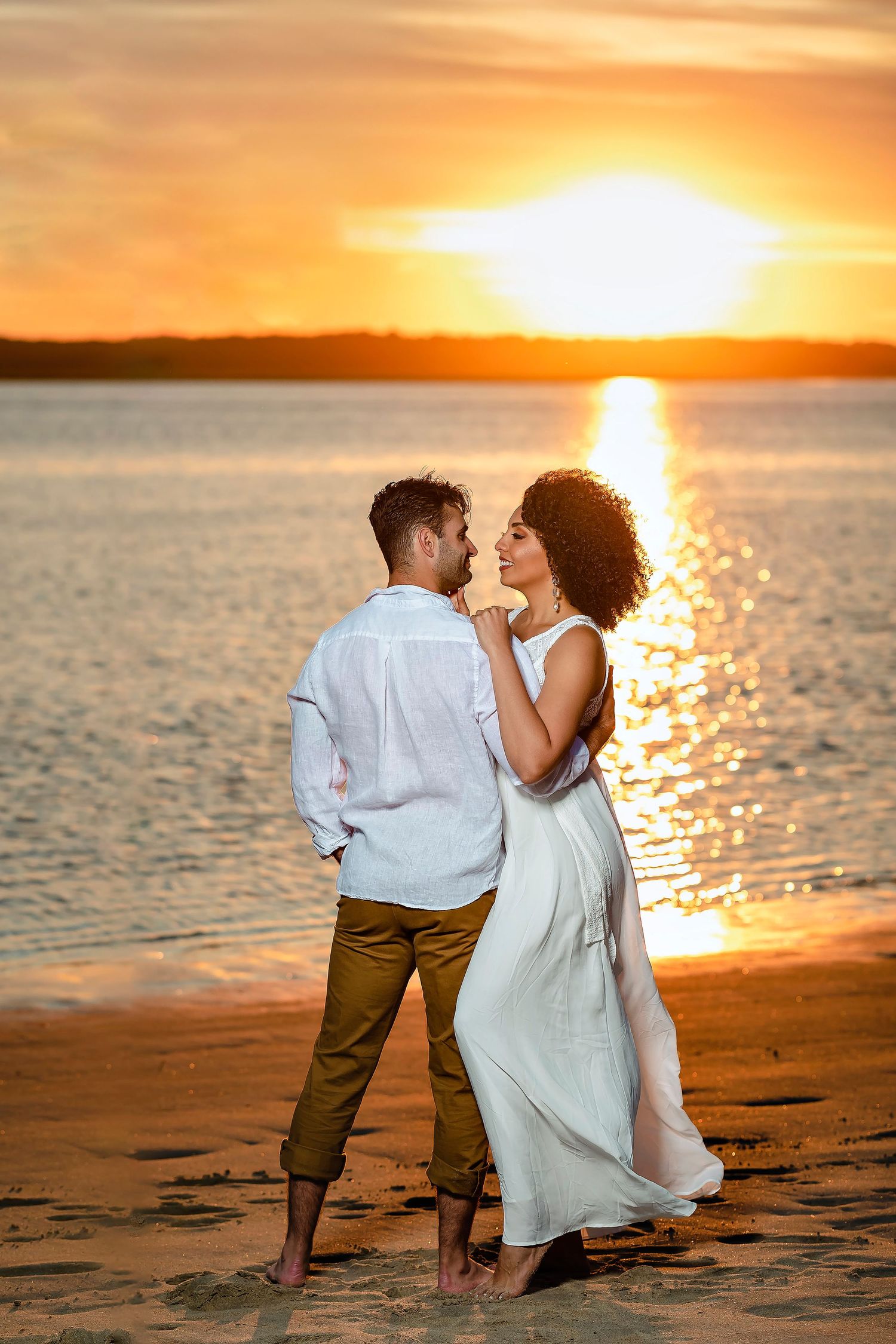 Intimate moments between couple on beach during dramatic orange sunset.
