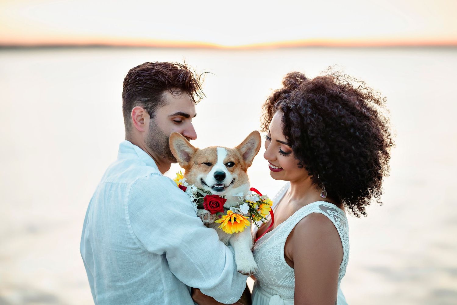 Couple joyfully poses with stuffed animal on beach at sunset.