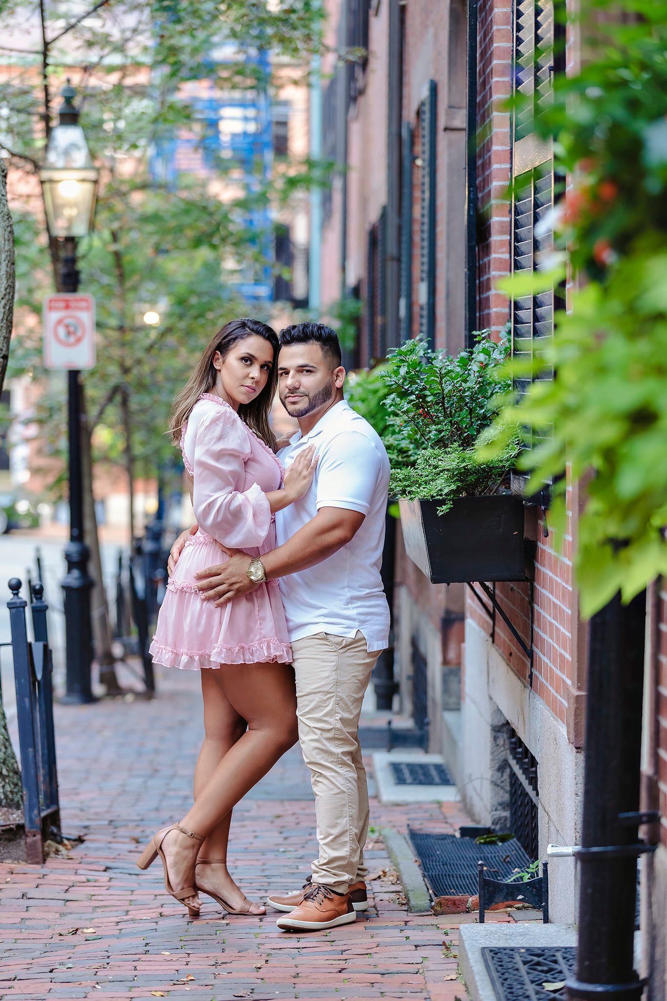 Couple in matching pink and white outfits posing playfully on brick sidewalk.