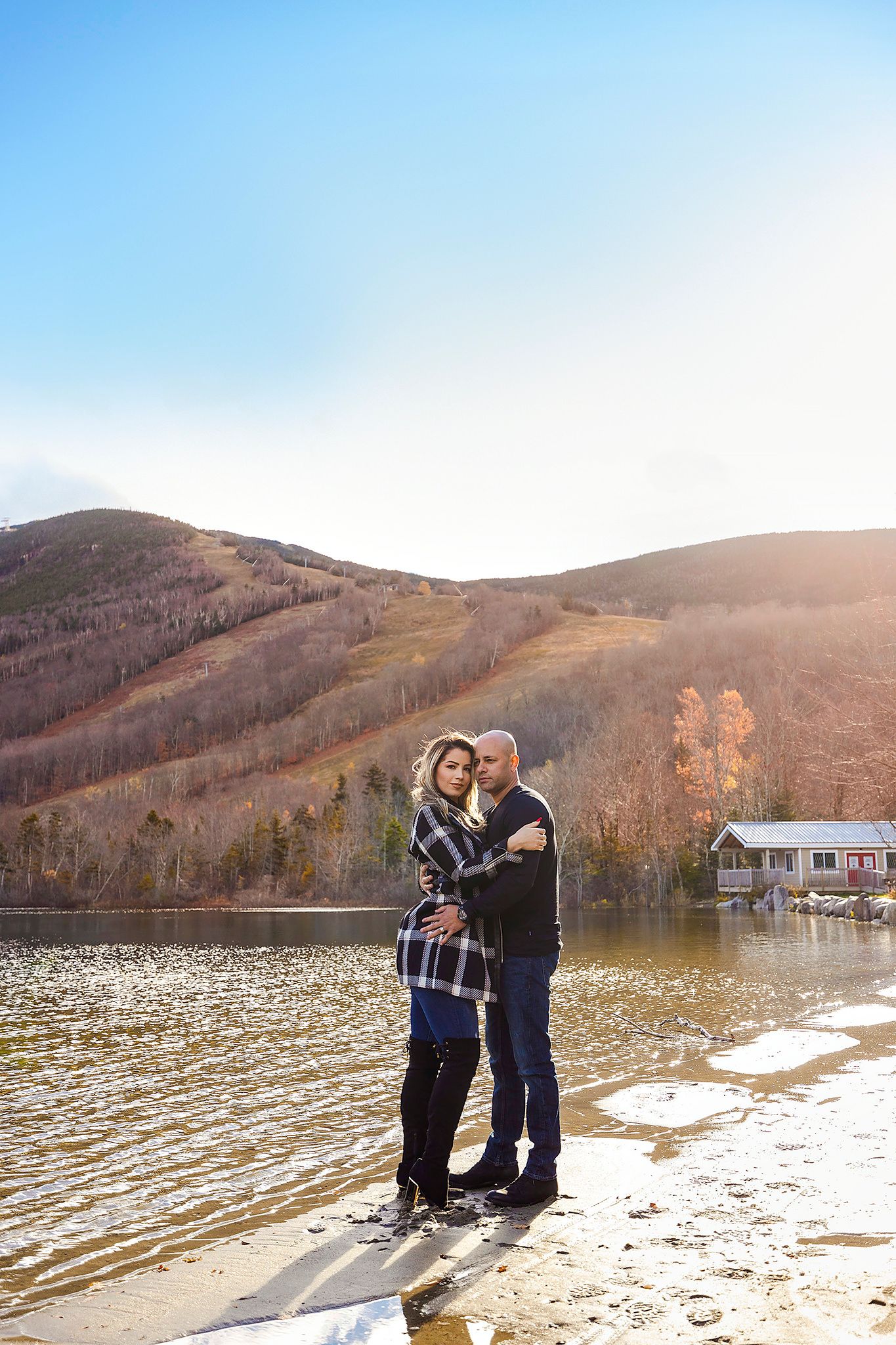 A romantic winter scene of a couple embracing by a lake with snow-covered mountains in the background.