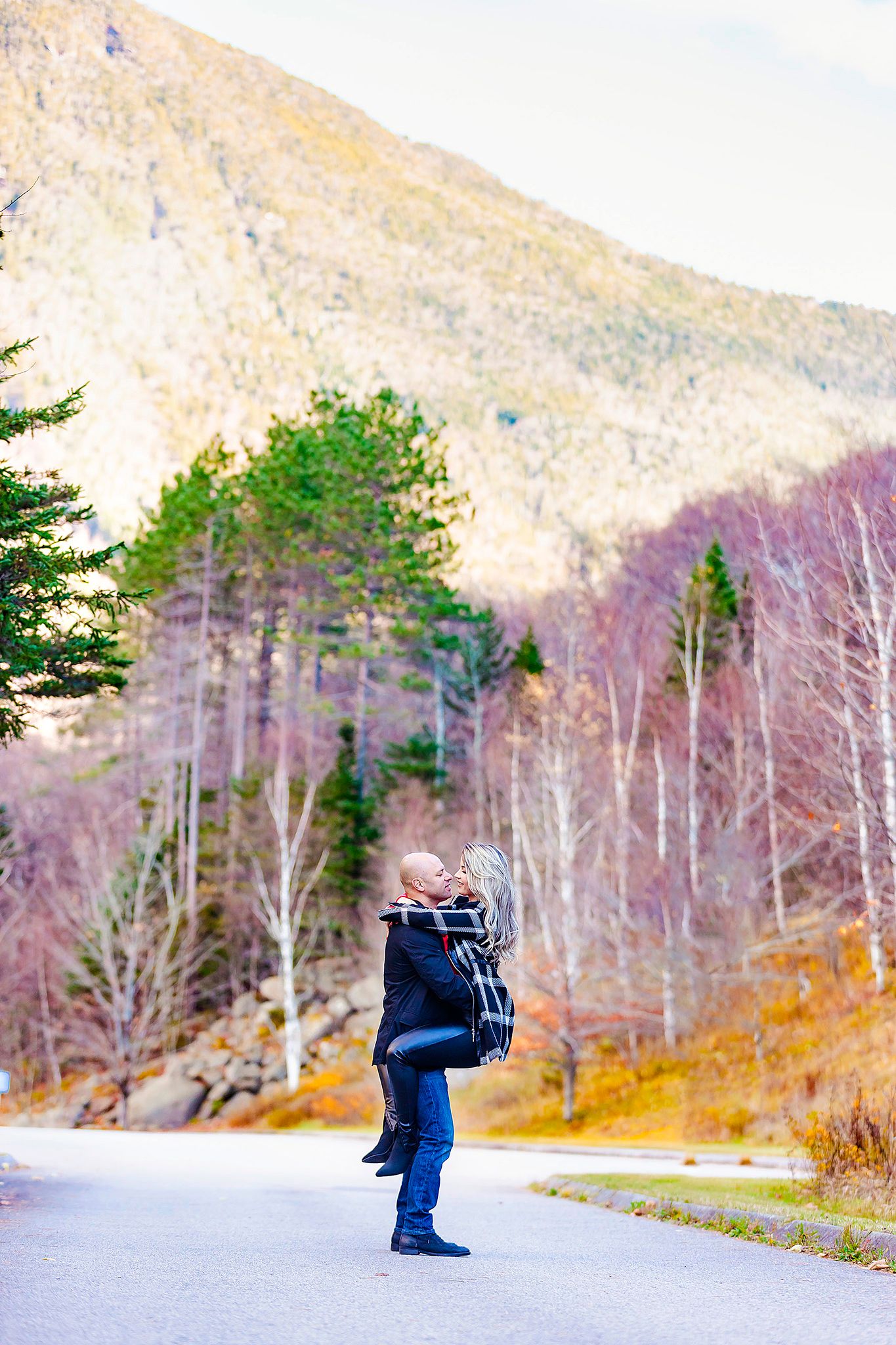 A silhouette figure stands on a mountain road surrounded by autumn foliage and tall peaks.