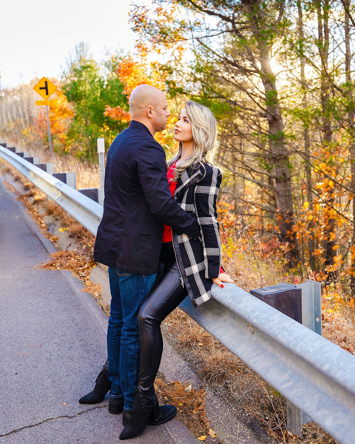 A romantic couple embraces by a guardrail on a scenic mountain road during autumn.