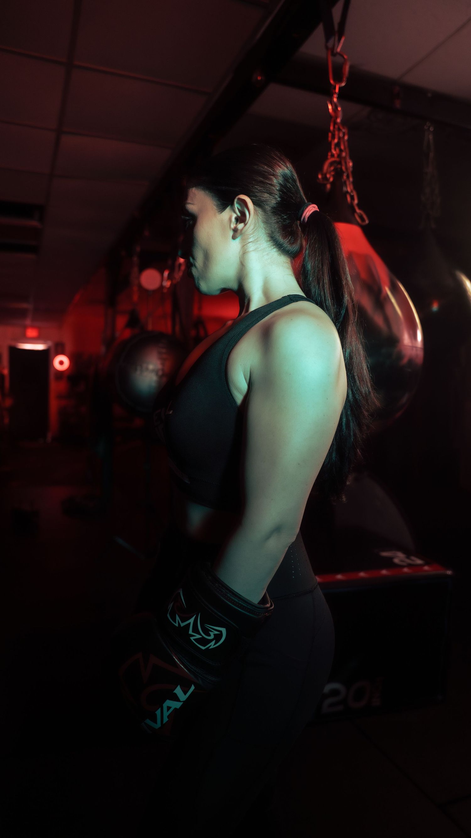 An athlete in dark workout attire trains in a dimly lit gym with red ambient lighting.