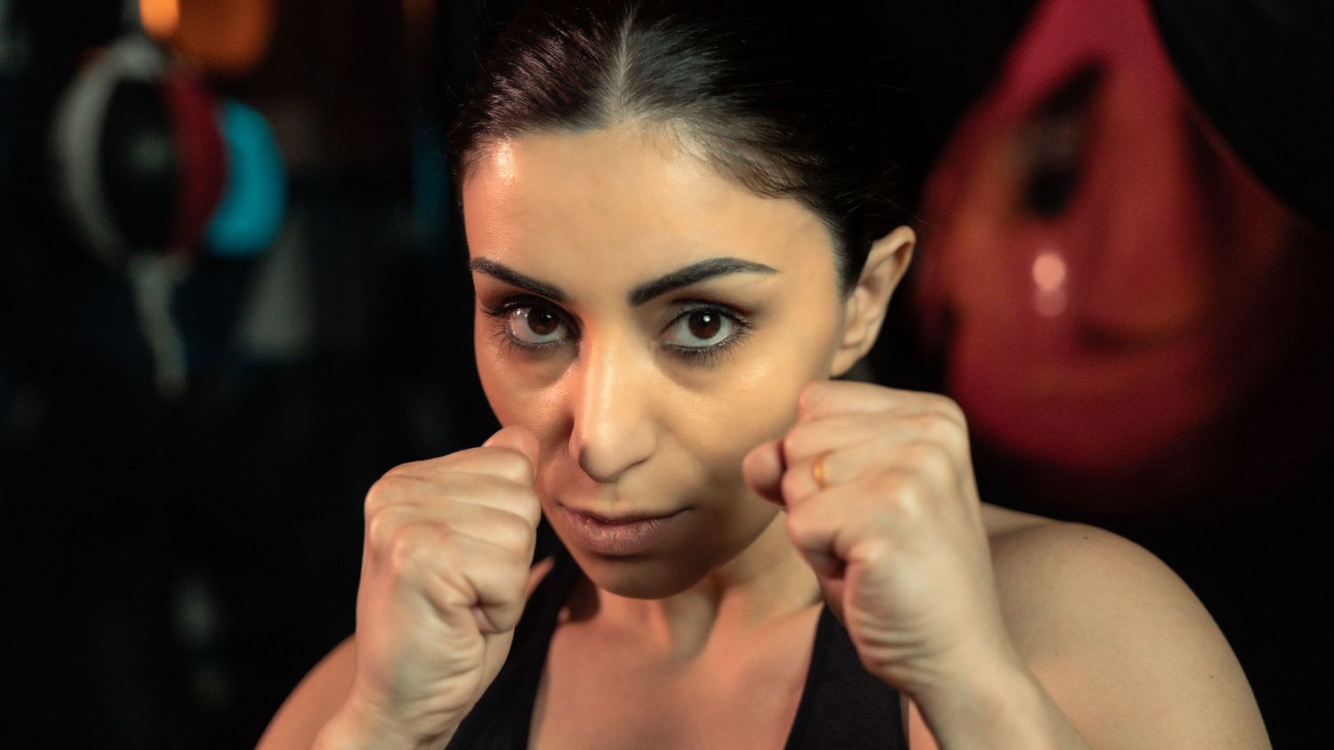 A boxer in a black tank top poses with raised fists in a fighting stance.