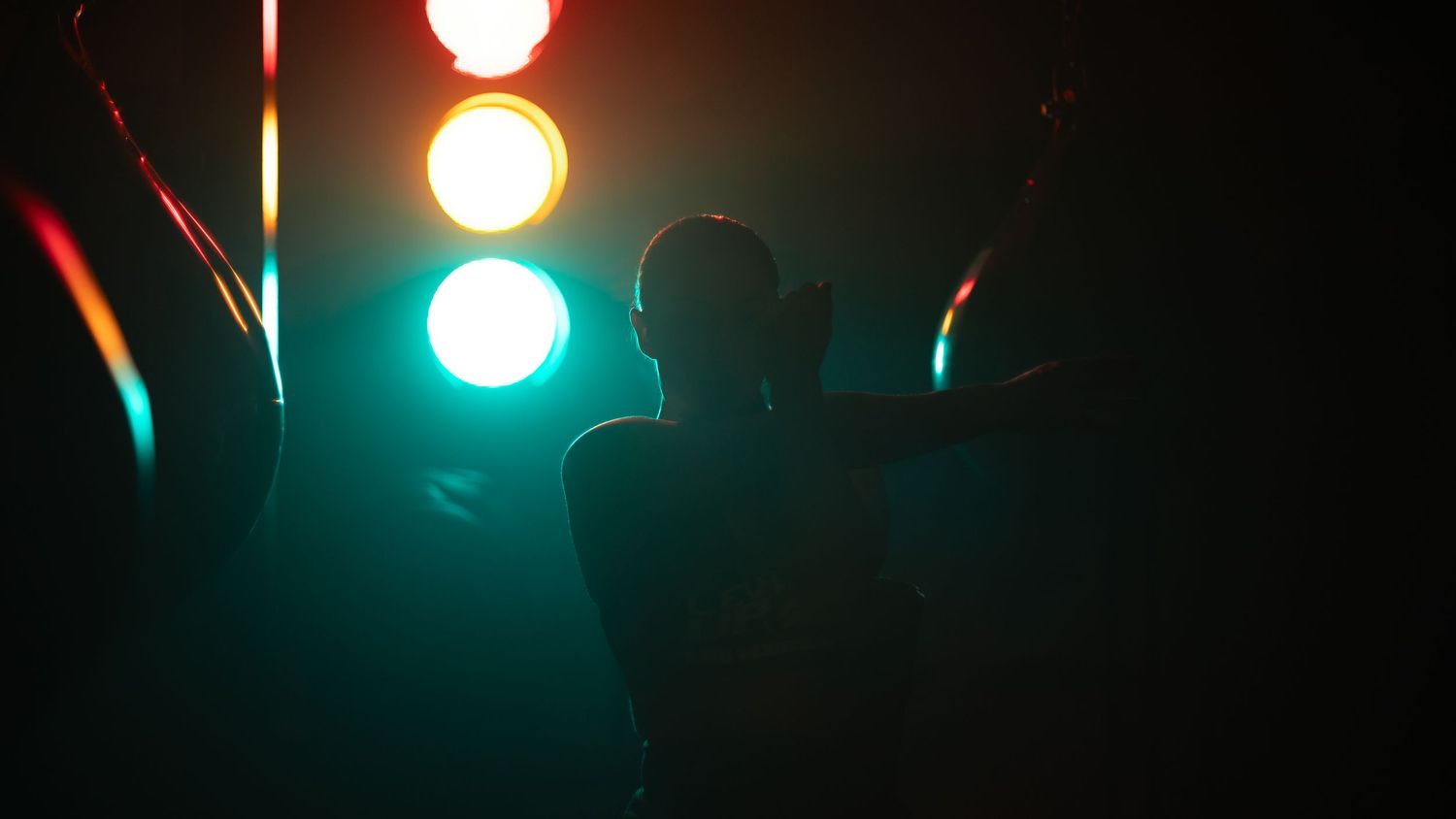 A silhouetted figure stands beneath colorful traffic light-style gym lighting.