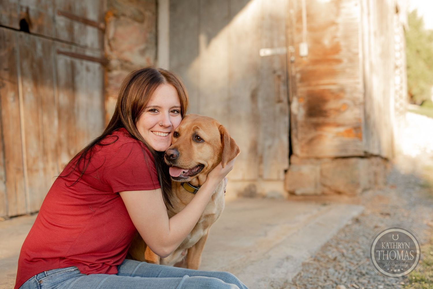 Person in red shirt hugging golden retriever dog by rustic stone wall.
