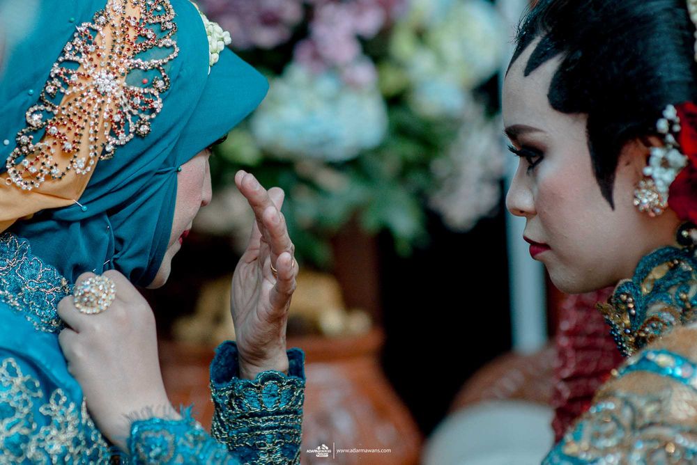 Intimate moment during traditional Indonesian wedding ceremony with ornate attire.