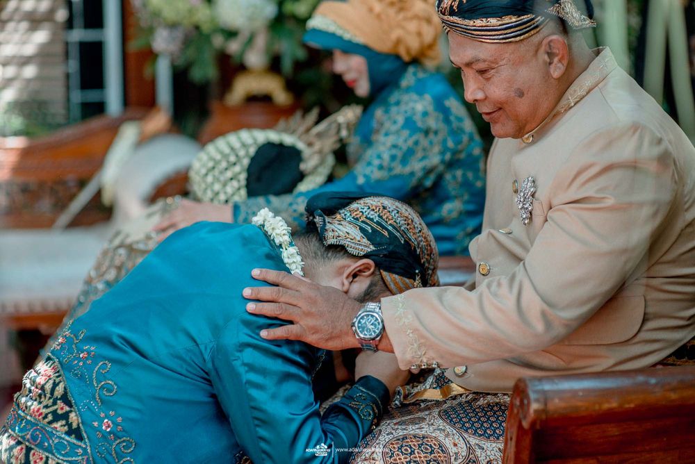Traditional Indonesian wedding ceremony shows gesture of respect with person bowing in colorful traditional attire.