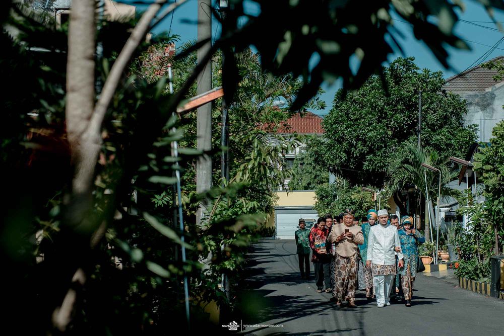 People walking down tree-lined street in traditional Indonesian attire.