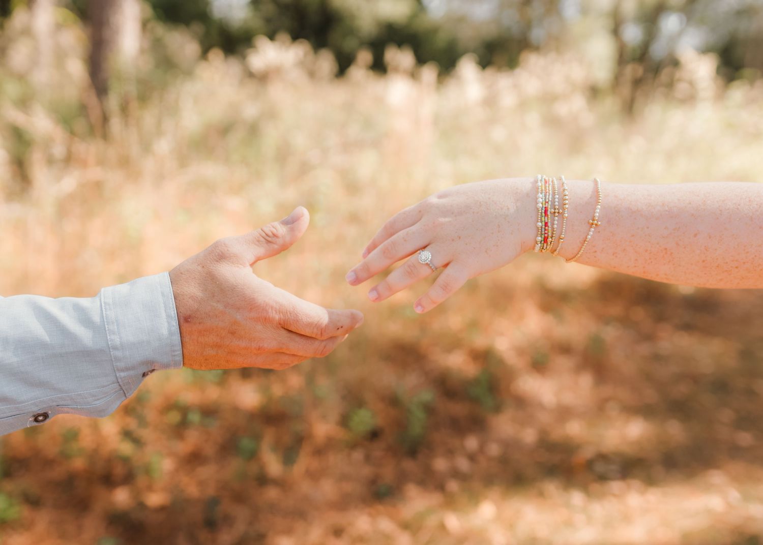 Two hands reaching toward each other in soft golden sunlight.
