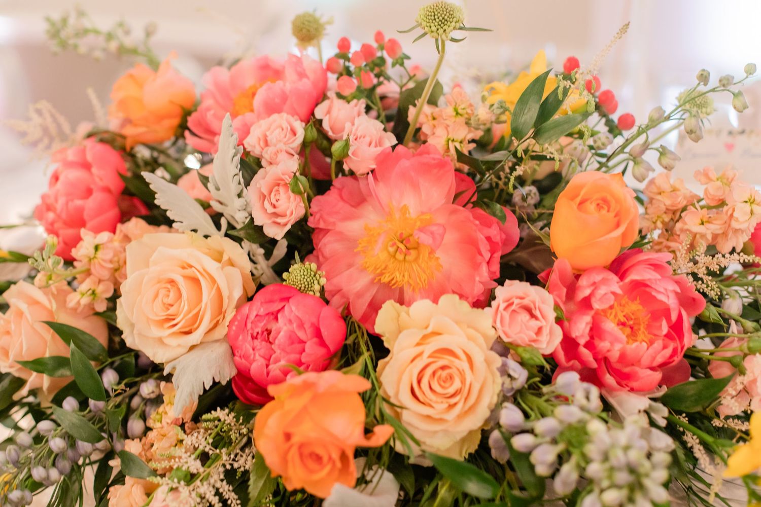 Lush coral and peach floral centerpiece arrangement with roses and greenery on wedding reception table.