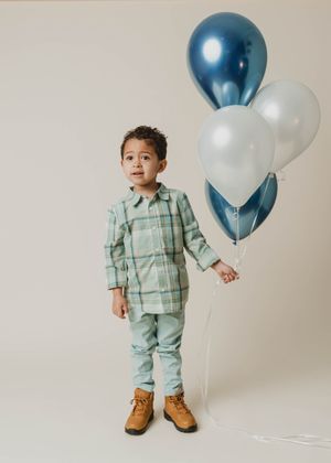 Young boy in plaid shirt holds blue and silver balloons in studio birthday portrait.