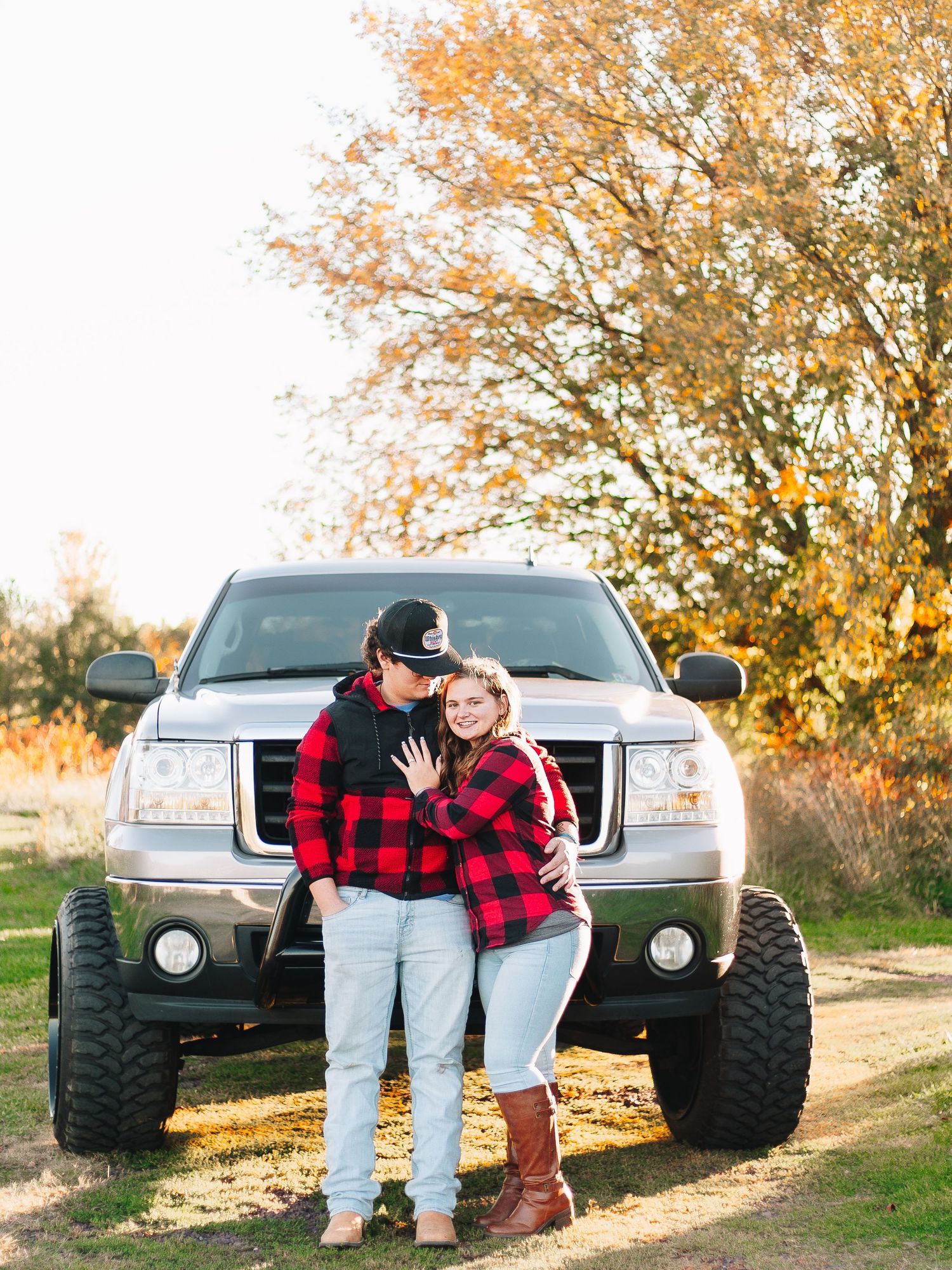 Couple standing in front of a lifted truck during golden hour wearing casual clothing.