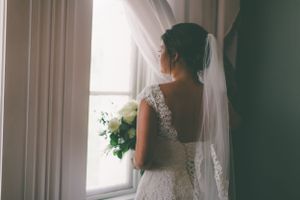 Back view of a lace wedding dress with delicate details and white rose bouquet.