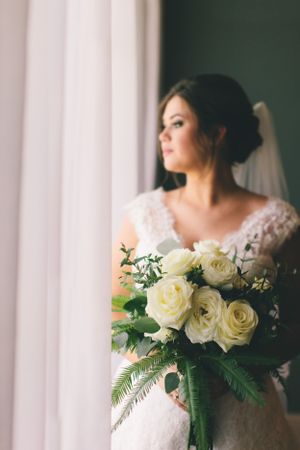Elegant bridal portrait with a stunning white rose bouquet by a window.