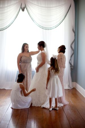 A bridal preparation scene with white dresses against draped curtains in soft light.