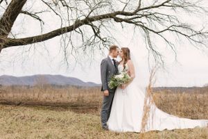 A romantic wedding portrait featuring a couple underneath a bare tree branch in a rustic field.