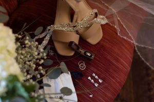 Wedding accessories including sparkly shoes, rings, and baby's breath flowers arranged on red fabric.