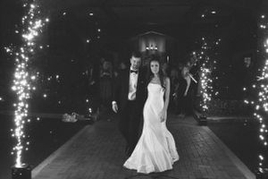 A black and white photo of a wedding couple walking down a path lined with sparklers.
