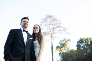 Low angle portrait of a couple against a bright sky with trees.