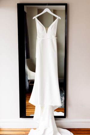 Elegant white wedding dress with plunging neckline hangs on display against a full-length mirror.