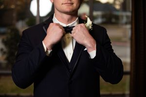 A groom adjusts his bowtie while wearing a classic black tuxedo.