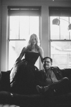 Artistic black and white portrait of two people lounging on a couch near bright windows.